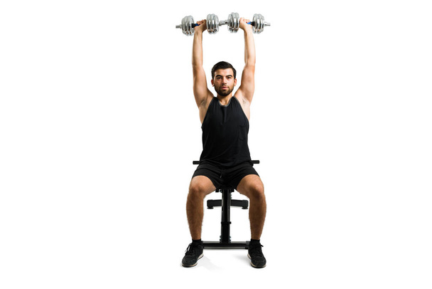 Active young man making eye contact while doing weight lifting with dumbbell isolated on a white studio background - Foto, Imagem