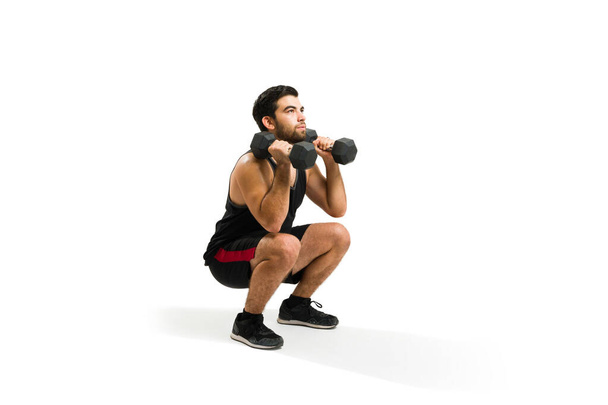 Strong young man doing squats and exercising with dumbbell weights during his workout routine - Photo, image