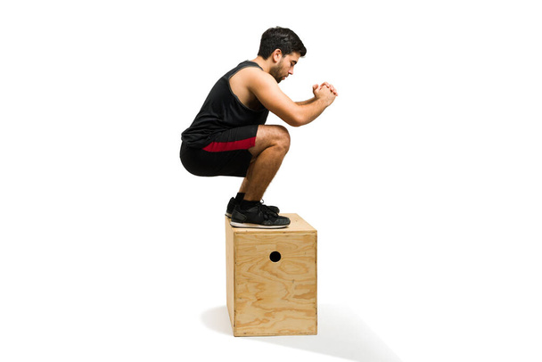 Active young man jumping on a plyo box and exercising with a cross training routine at the gym - Fotó, kép