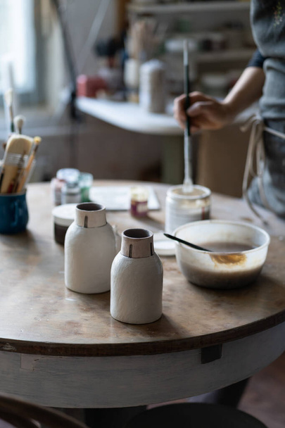 Crop photo of skilled master leaving clay vases to dry out on table after baking and handmade shaping in studio. Craftsworker hands put necessary appliances for painting vase on table in special shop - Foto, afbeelding