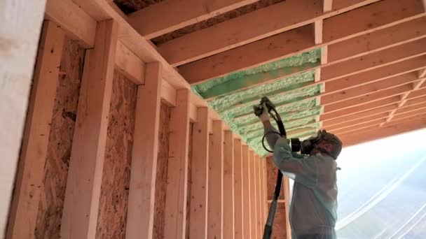 Male builder insulating wooden frame house. Man worker spraying polyurethane foam inside of future cottage, using plural component gun. Construction and insulation concept. - Filmati, video