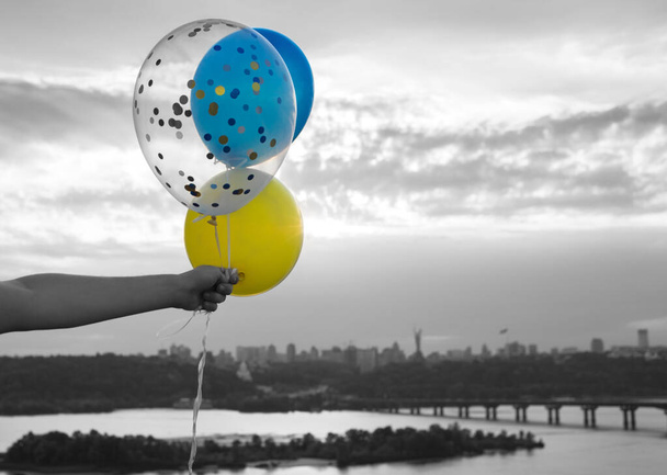 yellow and blue helium balloons in hand against sky and Dnieper river in Kyiv. color accent of flag of Ukraine. hopes for happiness during fighting on territory of Ukraine. Black and white photography - Foto, Imagen