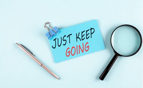 JUST KEEP GOING text written on a sticky with magnifier and pen, business concept - Foto, imagen