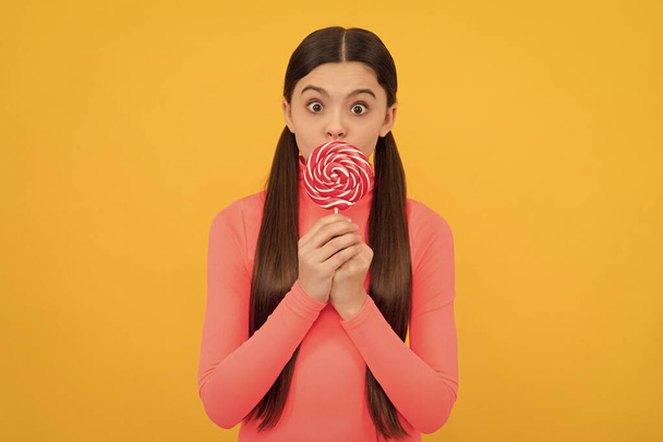 oh my god. teen dental care. sweet tooth. yummy. surprised girl hold lollipop. lollipop child. kid with long hair hold lollypop. sugar candy on stick. caramel candy shop. sweet childhood life. - Fotografie, Obrázek