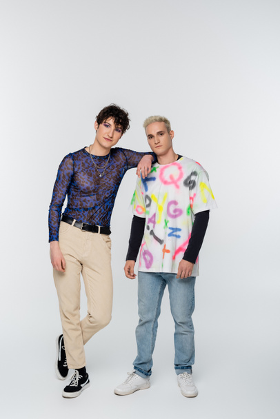 stylish queer person leaning on gay man while looking at camera on grey background - Fotoğraf, Görsel