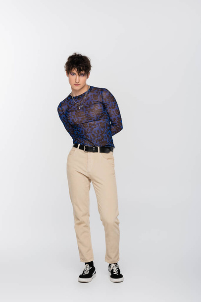 full length of queer person in beige trousers and spotty long sleeve shirt on grey background - Fotó, kép