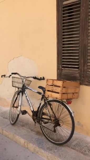 Vintage old bicycle with basket and wooden basket at the back on the typical Italian alley against yellow rustic wall - Felvétel, videó