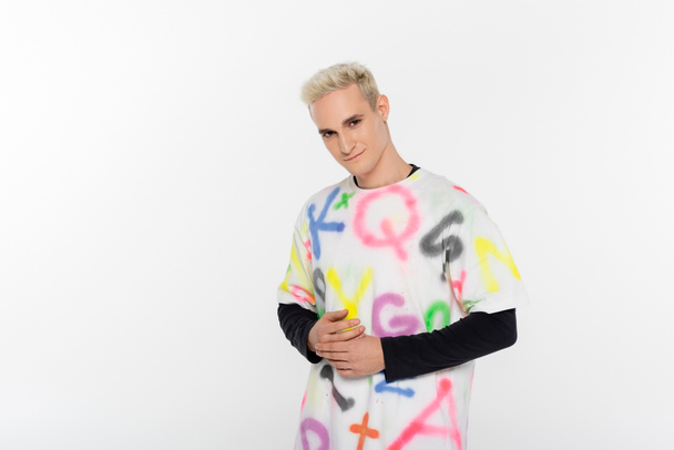 blonde gay man in fashionable t-shirt smiling at camera isolated on grey - Foto, Imagem