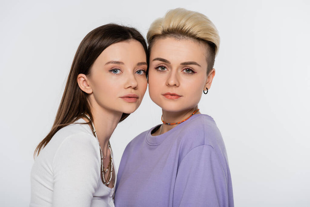 young and pretty lesbian couple  with beads and makeup looking at camera isolated on grey - Valokuva, kuva