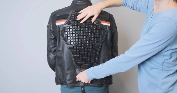 Woman applies a back protector to a leather motorcycle sport jacket worn by a biker. Moto accessories, saving the life of a motorcyclist. Fitting protection, rear view, close-up. High quality photo - Fotó, kép