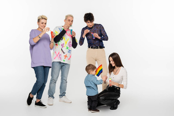 young lgbtq community friends blowing soap bubbles near toddler boy on grey background - Foto, afbeelding