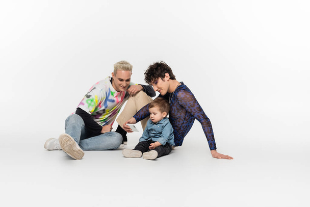 happy gay men sitting with toddler kid and taking selfie on smartphone on grey background - Fotoğraf, Görsel