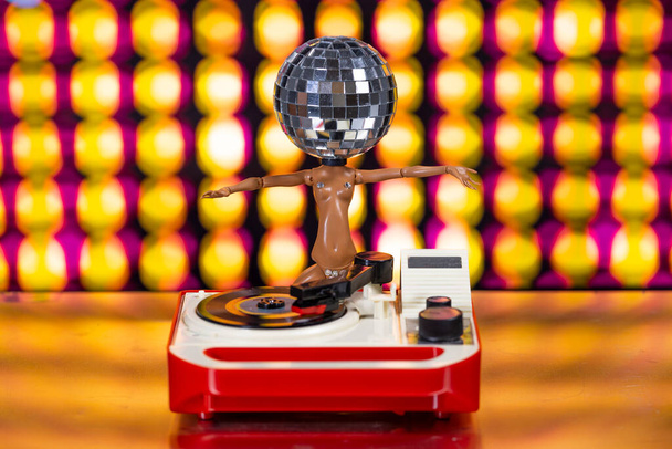 A sparkling DJ doll with a discoball head dances with a record turntable  - Foto, Bild