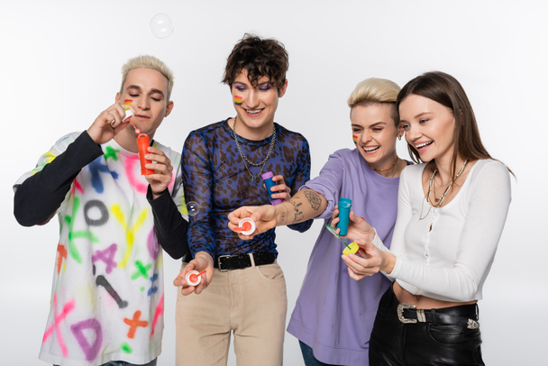 excited lgbtq community friends in stylish clothes blowing soap bubbles isolated on grey - Foto, Imagen