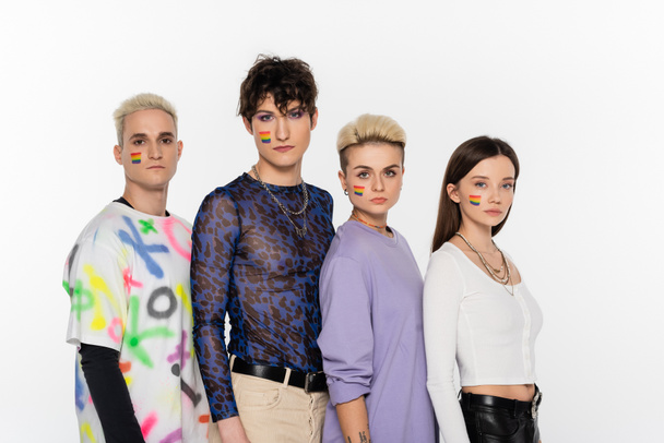 young and stylish people of different identity and with rainbow flags on faces looking at camera isolated on grey - Foto, Imagen