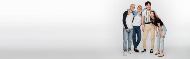 full length of trendy friends laughing and looking at camera on grey background, banner - Fotó, kép