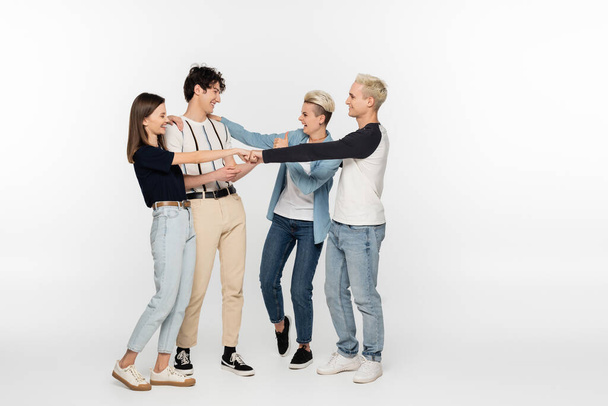 full length of young friends doing fist bump and showing thumb up on grey background - 写真・画像
