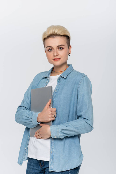 young and stylish woman with laptop looking at camera isolated on grey - Foto, Bild