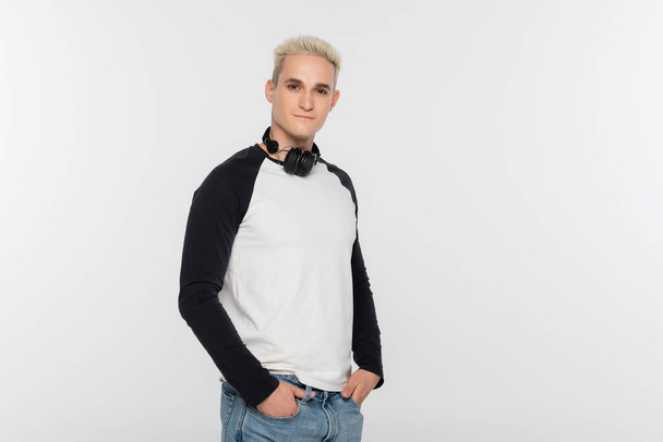trendy man in black and white long sleeve shirt standing with wireless headphones isolated on grey - Photo, Image