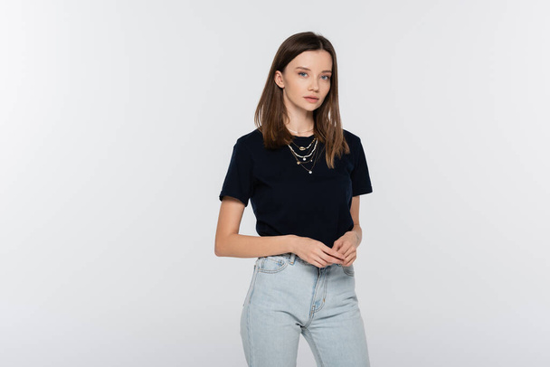 brunette woman in jeans and black t-shirt looking at camera isolated on grey - Foto, Imagen