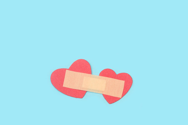An adhesive bandage uniting two red paper hearts on a light blue background with copy space - Fotó, kép