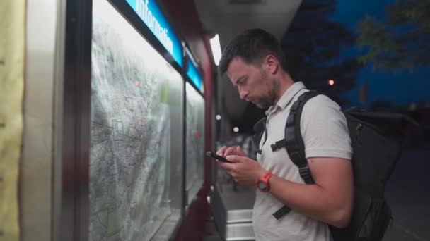 Male passenger analyzes transport card at a public transportation stop and matches it to an app on his phone in Munich, Germany. Checking map and waiting for transport in city. Public transport route - Materiaali, video