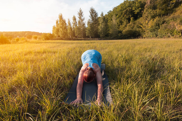 girl of fair appearance with tied hair,dressed in blue clothes for phineas,does yoga outdoors at sunset.healthy lifestyle concept,there is a place for an inscription. High quality photo - Fotó, kép
