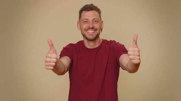 Like. Bearded handsome young man raises thumbs up agrees with something or gives positive reply recommends advertisement likes good. Adult stylish guy isolated alone on beige studio background indoors - 写真・画像
