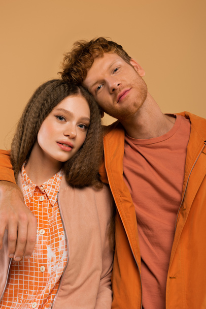 redhead young man in orange jacket hugging girlfriend isolated on beige - Fotó, kép