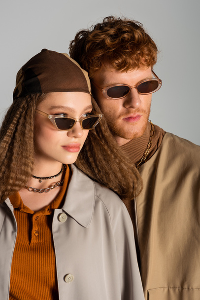 portrait of young stylish couple in autumnal outfits and sunglasses posing isolated on grey - Fotografie, Obrázek
