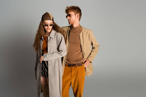 young stylish couple in autumnal outfits and sunglasses posing on grey - Φωτογραφία, εικόνα