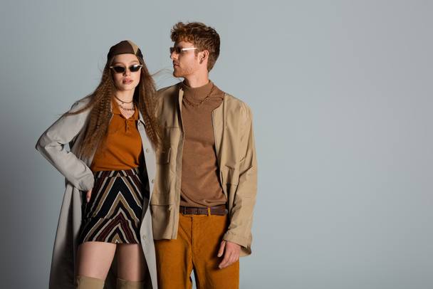 stylish couple in autumnal outfits and trendy sunglasses standing isolated on grey - Fotó, kép