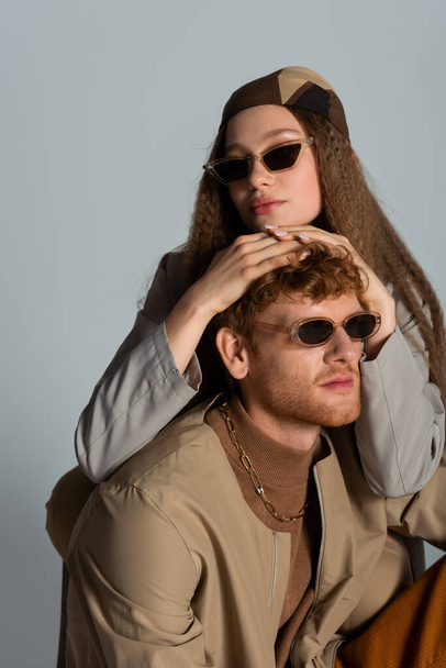 young and stylish couple in sunglasses and autumnal clothes posing isolated on grey - Foto, immagini