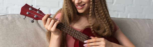 cropped view of happy teenage girl in casual clothes playing ukulele, banner - Foto, afbeelding