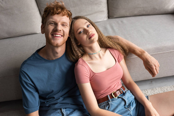 high angle view of young couple smiling while sitting near couch in modern living room - Foto, afbeelding
