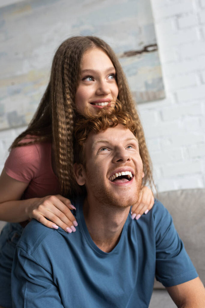 happy teen girl smiling and hugging excited boyfriend in living room - Фото, изображение