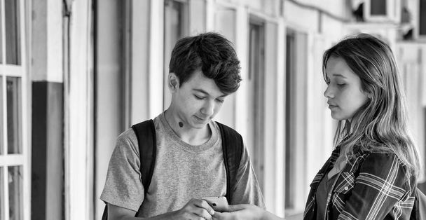 Caucasian teenager couple slooking to the smartphone in the school hallway. - Photo, Image