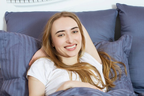 mooie blonde vrouw liggend in bed, mooie blonde poseren in een slaapkamer - Foto, afbeelding