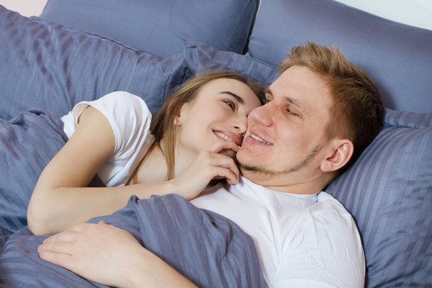 Hermosa pareja amorosa despertada en la cama por la mañana. Joven pareja heterosexual adulta acostada en la cama en el dormitorio. - Foto, imagen