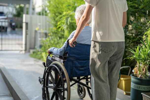 Pflegerin hilft und pflegt asiatische Seniorin oder ältere Dame Patientin im Rollstuhl an Rampe in Pflegeheim, gesundes starkes medizinisches Konzept. - Foto, Bild
