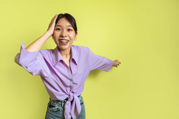 Возбужденная азиатская женщина указывает на Aside касаясь головы реклама Wow Предложение на жёлтом фоне в студии. Женщина, показывающая космическую улыбку на камеру. "Look There Concept". Селективный фокус - Фото, изображение