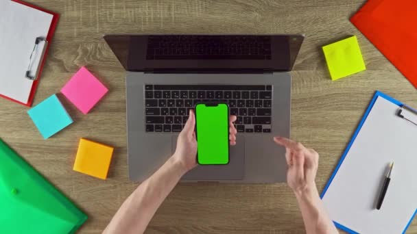 Freelancer is showing on the phone in vertical position how easy to earn money with freelance green screen mockup. Laptop, color stickers and notebooks. - Metraje, vídeo