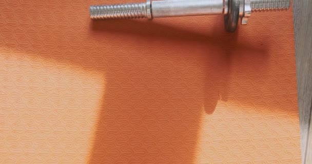 Disassembled metal dumbbell lies on an orange yoga mat in the room. Disassembled metal dumbbell lies on an orange yoga mat in the room. Top view. High quality 4k footage - Video