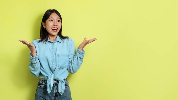Excited Korean Female Looking Aside Advertising Great Offer Standing On Yellow Background In Studio. Advertisement Banner. Panorama With Empty Space For Text - Foto, afbeelding