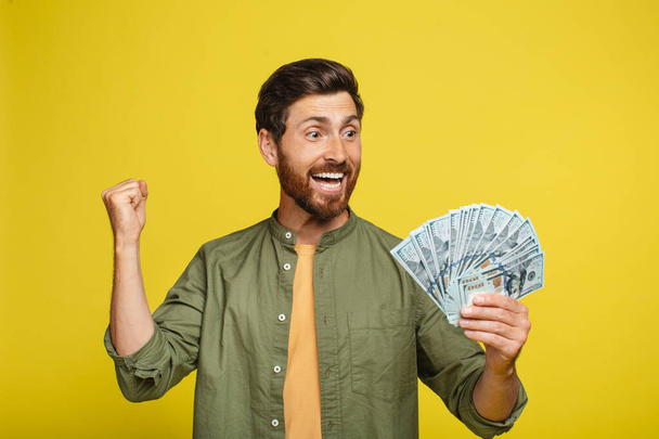 Overjoyed middle aged man holding lots of money, gesturing YES, male with fan of dollars showing casino or lottery win, achieving financial success over yellow studio background - Zdjęcie, obraz