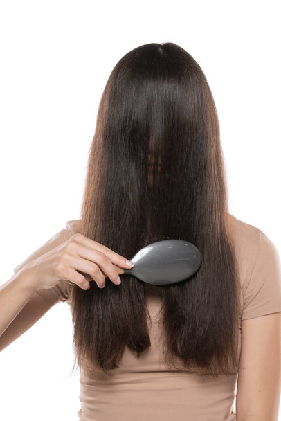 Μια γυναίκα χτενίζει τα μαλλιά πάνω από το πρόσωπό της σε λευκό φόντο στούντιο. - Φωτογραφία, εικόνα