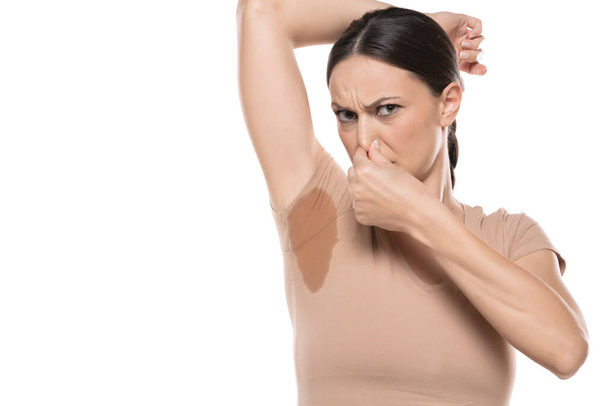 Νεαρή γυναίκα χέρι πιέζοντας τη μύτη με την οσμή του ιδρώτα, θηλυκό μυρίζοντας ή μυρίζοντας τη μασχάλη της, κακή μυρωδιά. - Φωτογραφία, εικόνα