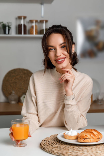beautiful young brunette girl in the kitchen in a sweater with lemon. beautiful smile. - Photo, Image