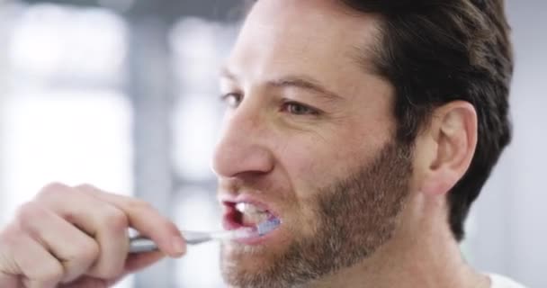Мужчина чистит зубы для стоматологического здравоохранения, очищает рот зубной щеткой и делает оздоровление для здоровья и гигиены в ванной комнате дома утром. Лицо и голова человека с улыбкой для ухода. - Кадры, видео