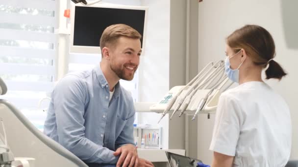Positive young man in consultation with a dentist in a modern dental office. Timely dental treatment - Záběry, video